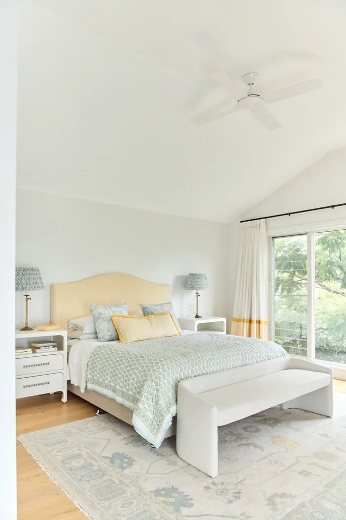 Elegant bedroom with a large bed, patterned bedding, two nightstands, and a window view of greenery.
