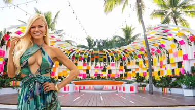 Colorful outdoor firepit area in the Love Island USA villa with vibrant panels, tropical plants, and an orange semicircular bench. Palm trees in the background. A photo of Sophie Monk has been placed in front and to the left.