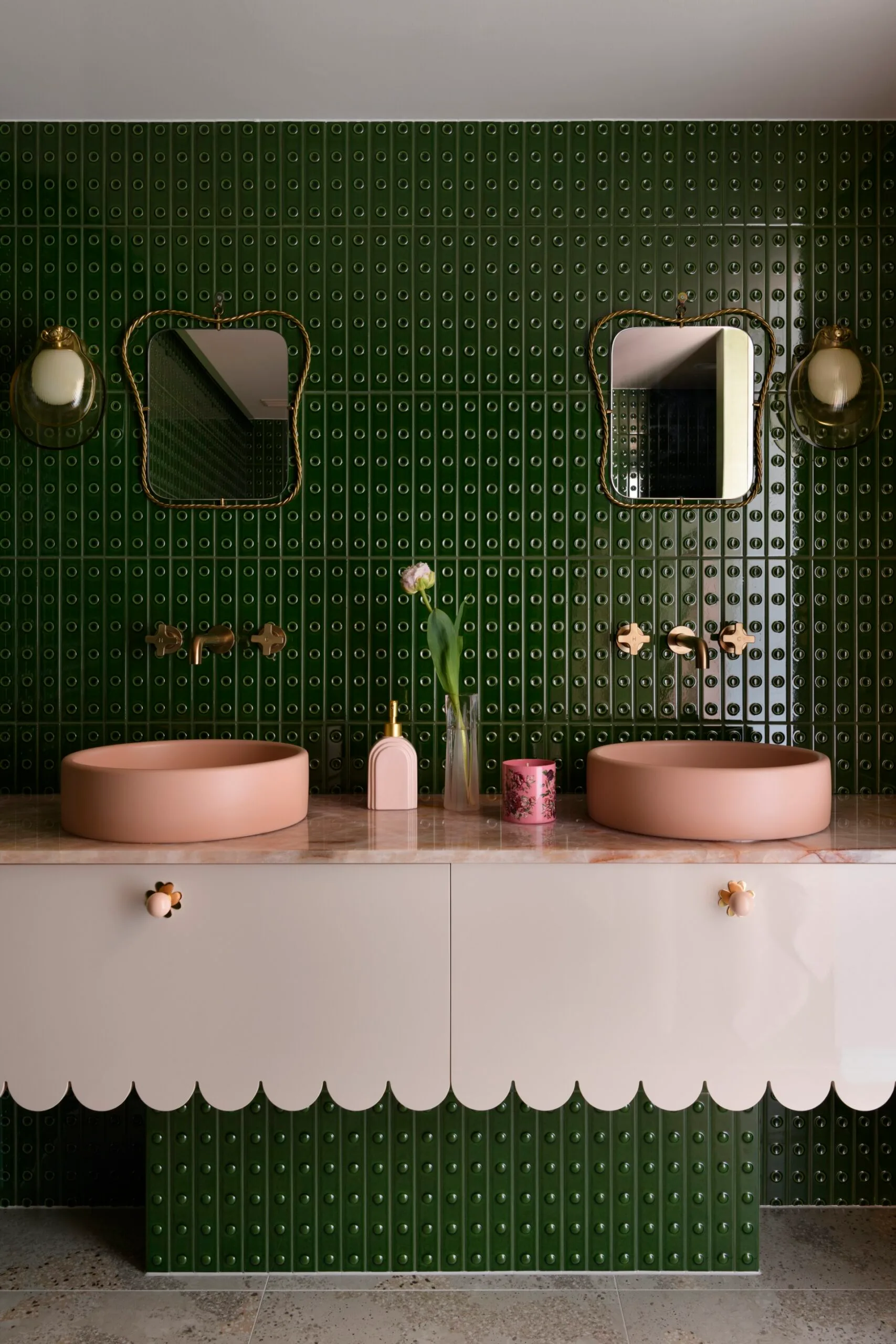 Modern bathroom with green tiled wall, two pink vessel sinks, scalloped cabinet, and decorative mirrors.