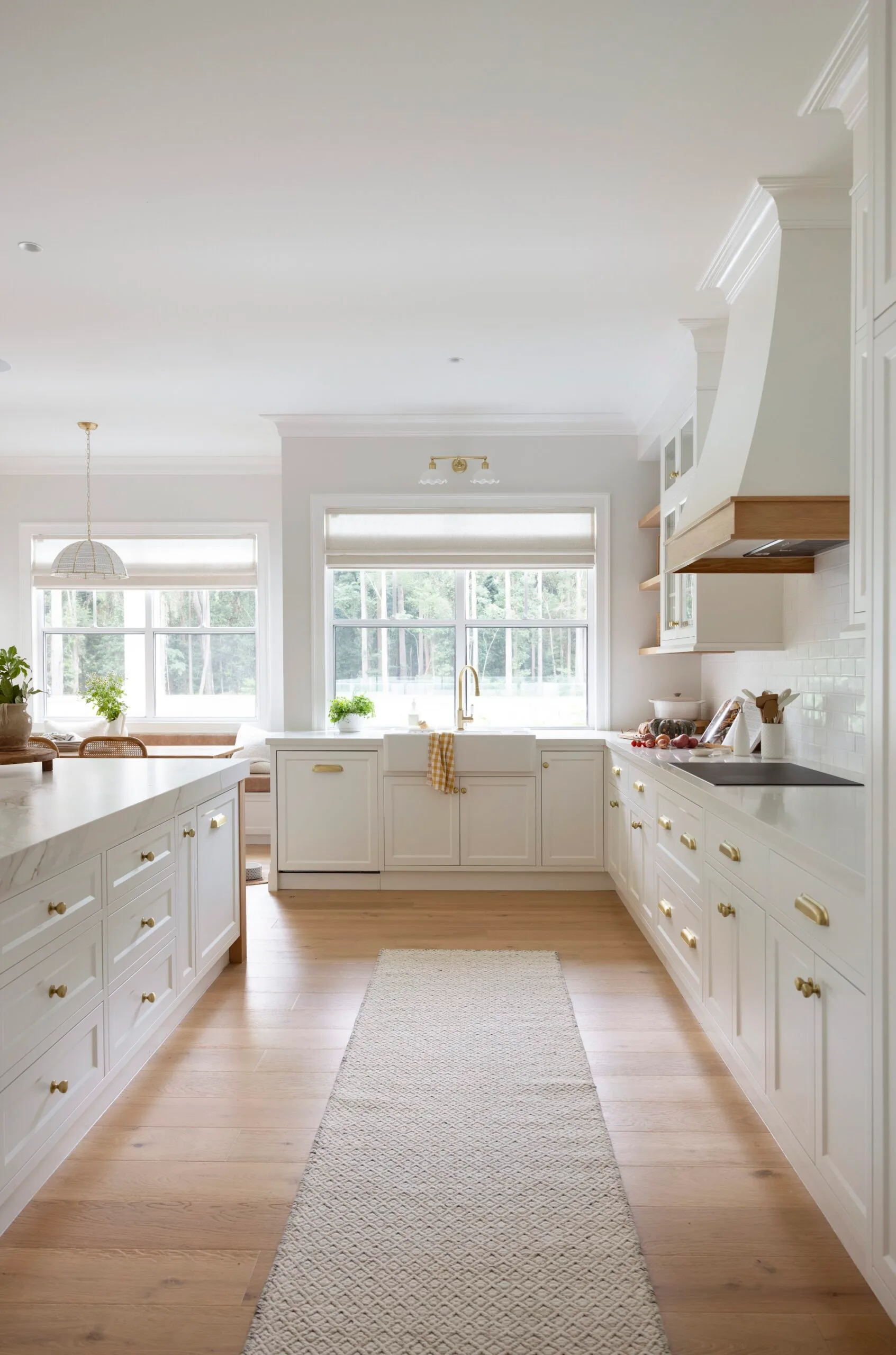 Bright, spacious kitchen with white cabinetry, large windows, and gold accents. Light wood flooring and a center island.