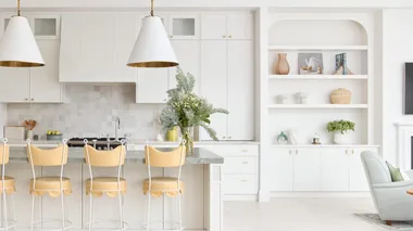 Bright, modern kitchen with white cabinetry, island with yellow stools, pendant lights, and built-in shelf decor.