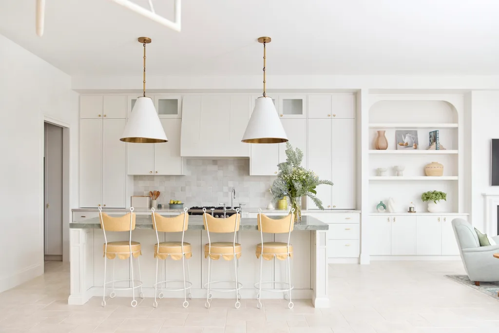 Bright, modern kitchen with white cabinetry, island with yellow stools, pendant lights, and built-in shelf decor.
