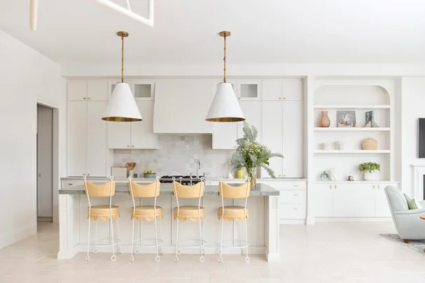 Bright, modern kitchen with white cabinetry, island with yellow stools, pendant lights, and built-in shelf decor.