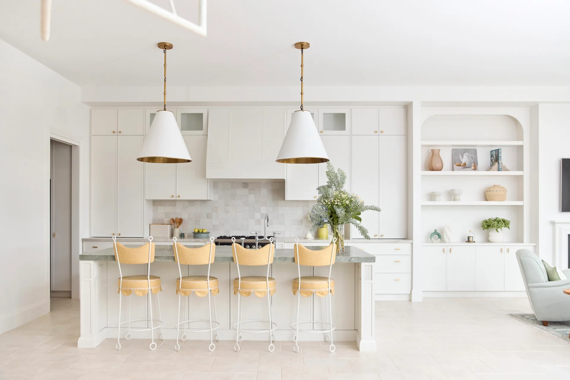 Bright, modern kitchen with white cabinetry, island with yellow stools, pendant lights, and built-in shelf decor.