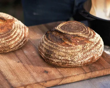 Two round loaves of wood-fired sourdough bread on a rustic wooden chopping board