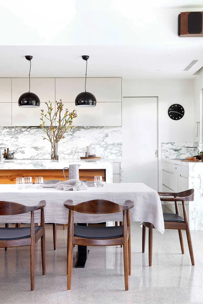 a white kitchen and dining area with shiny tiles black pendant lights and timber seating