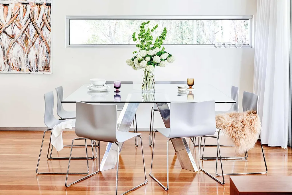 Glass dining table with white chairs and flowers