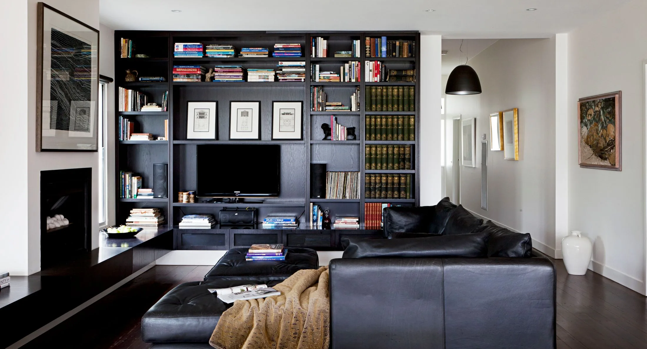 Living room with black leather sofa, bookshelf full of books, wall art, and a modern design.
