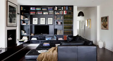 Living room with black leather sofa, bookshelf full of books, wall art, and a modern design.