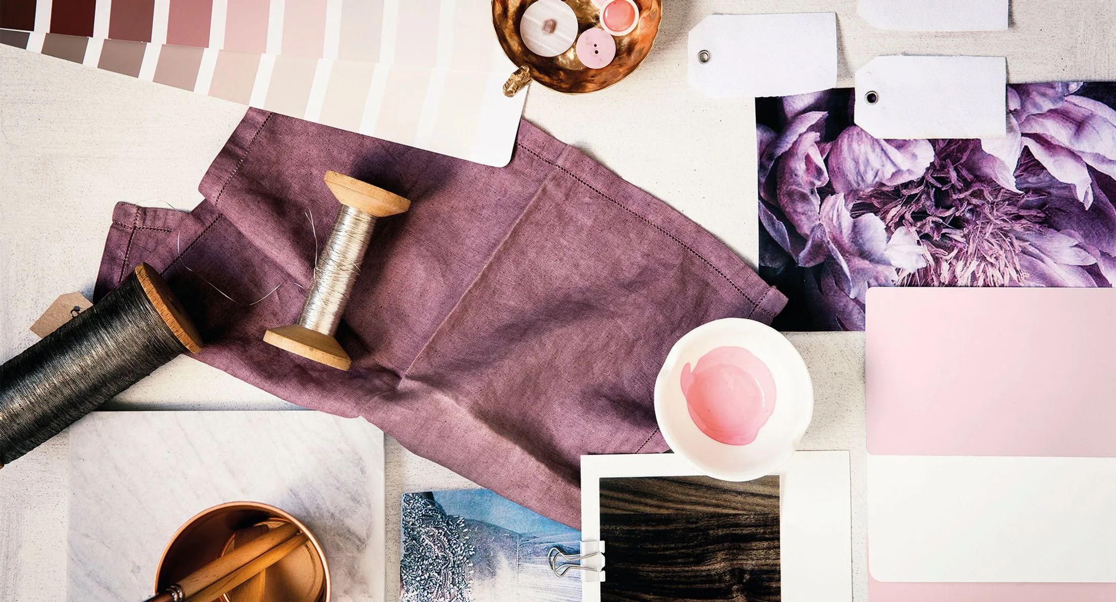 Fabric swatches, thread spools, paint cards, and pink flower photo on crafting table.