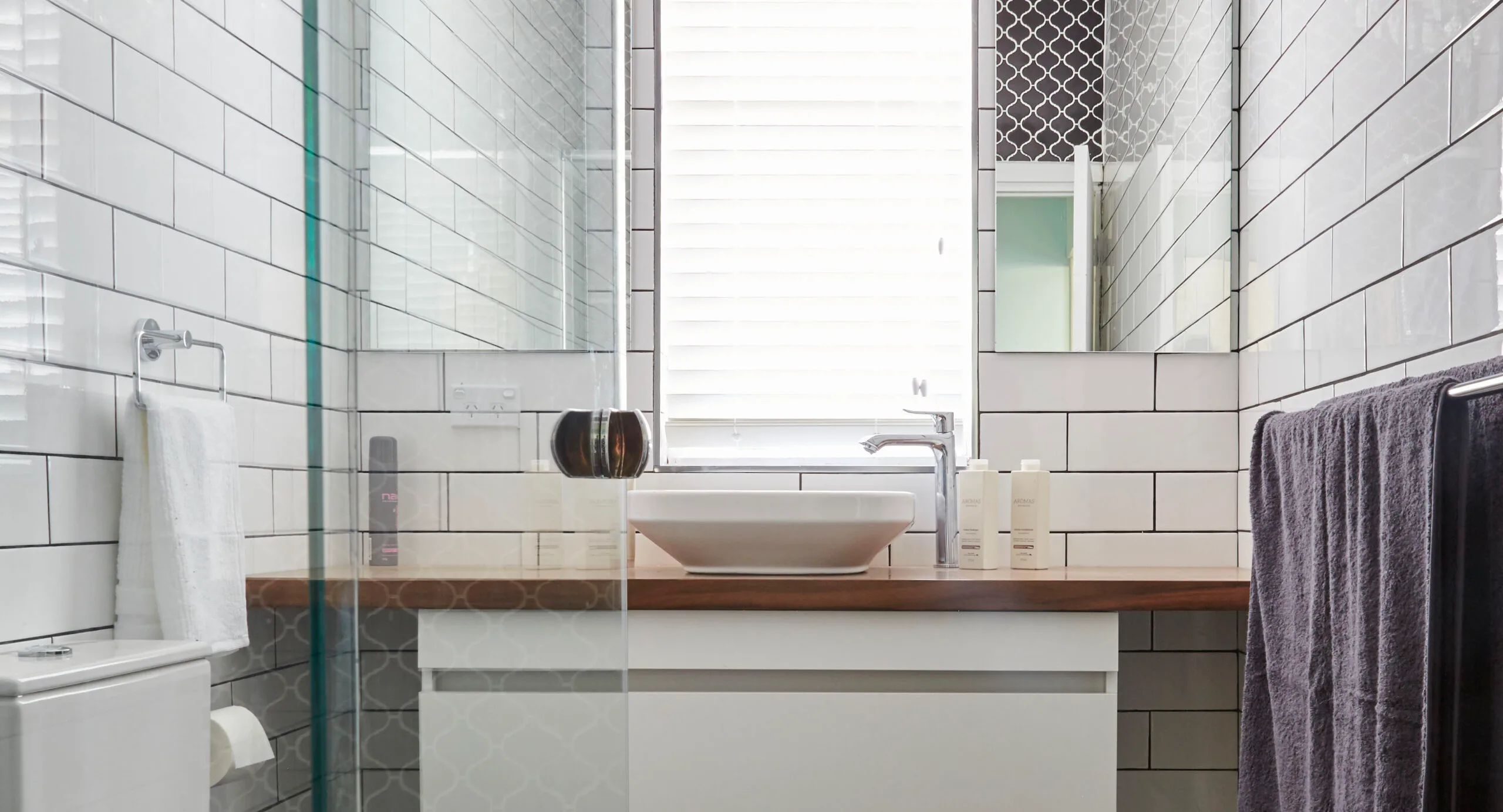 Modern bathroom with white subway tiles, wooden countertop, vessel sink, and towel rack.