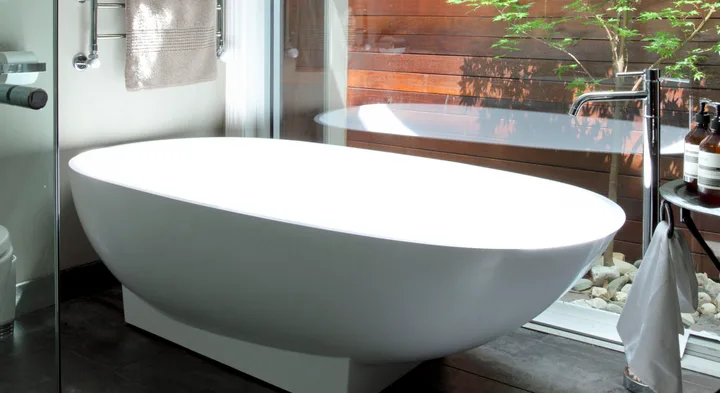 Freestanding white bathtub beside glass window with towel and toiletries nearby.