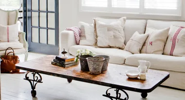 Cozy living room with cream sofa, rustic coffee table, wooden floor, books, and decorative pillows.
