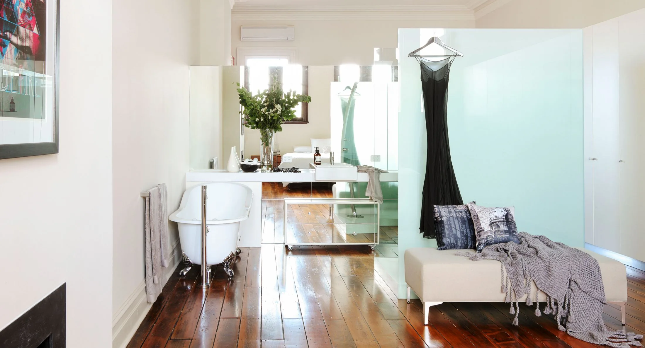 Luxurious bathroom with bathtub, elegant black dress hanging, modern sink, vase with greenery, and cozy seating area.