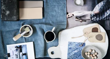 Coffee mug, paintbrush, tags, and photos on a blue fabric background arranged artistically.