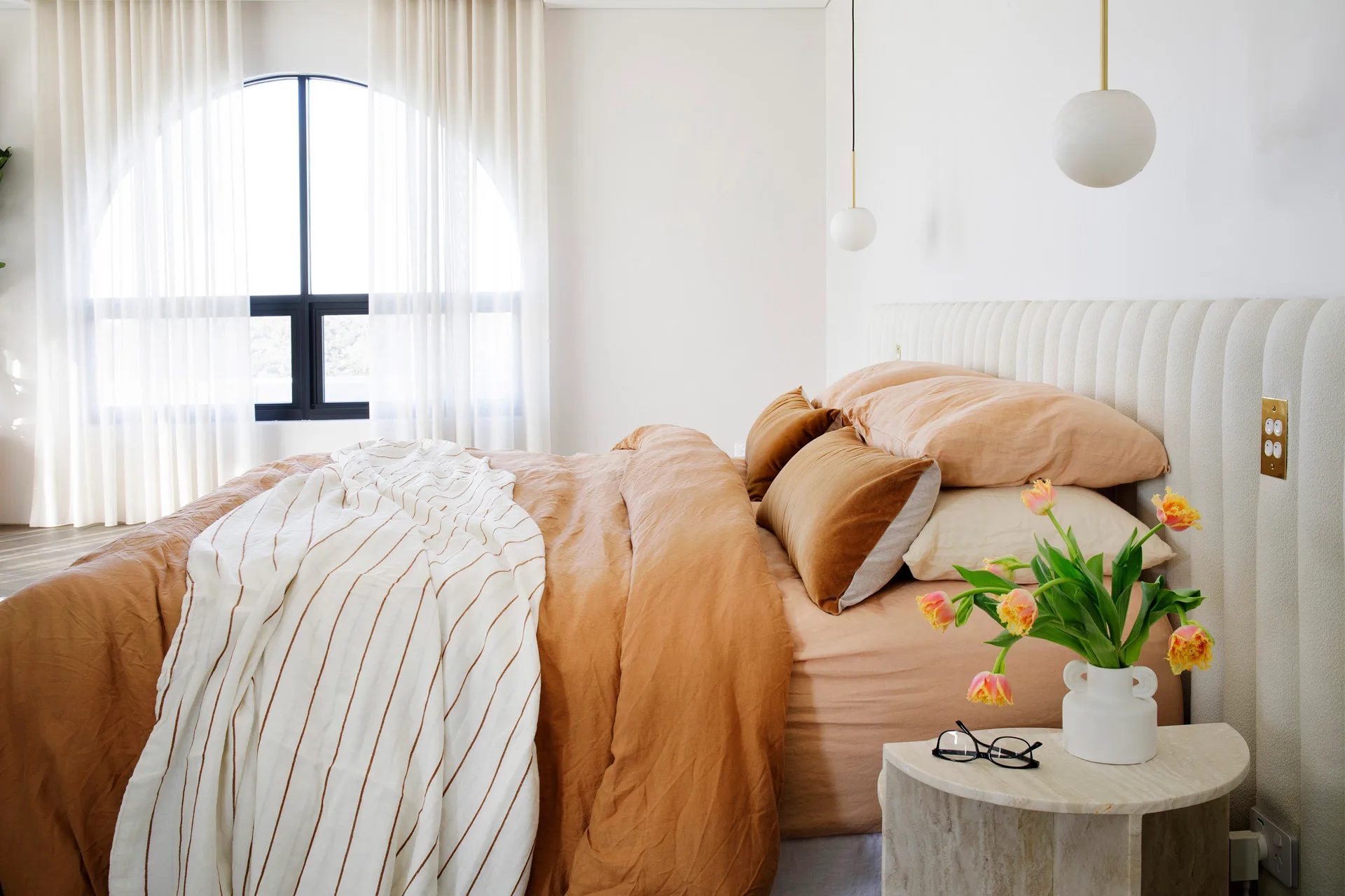 main bedroom with panelled white upholstered bedhead and arched windows and pendant lights