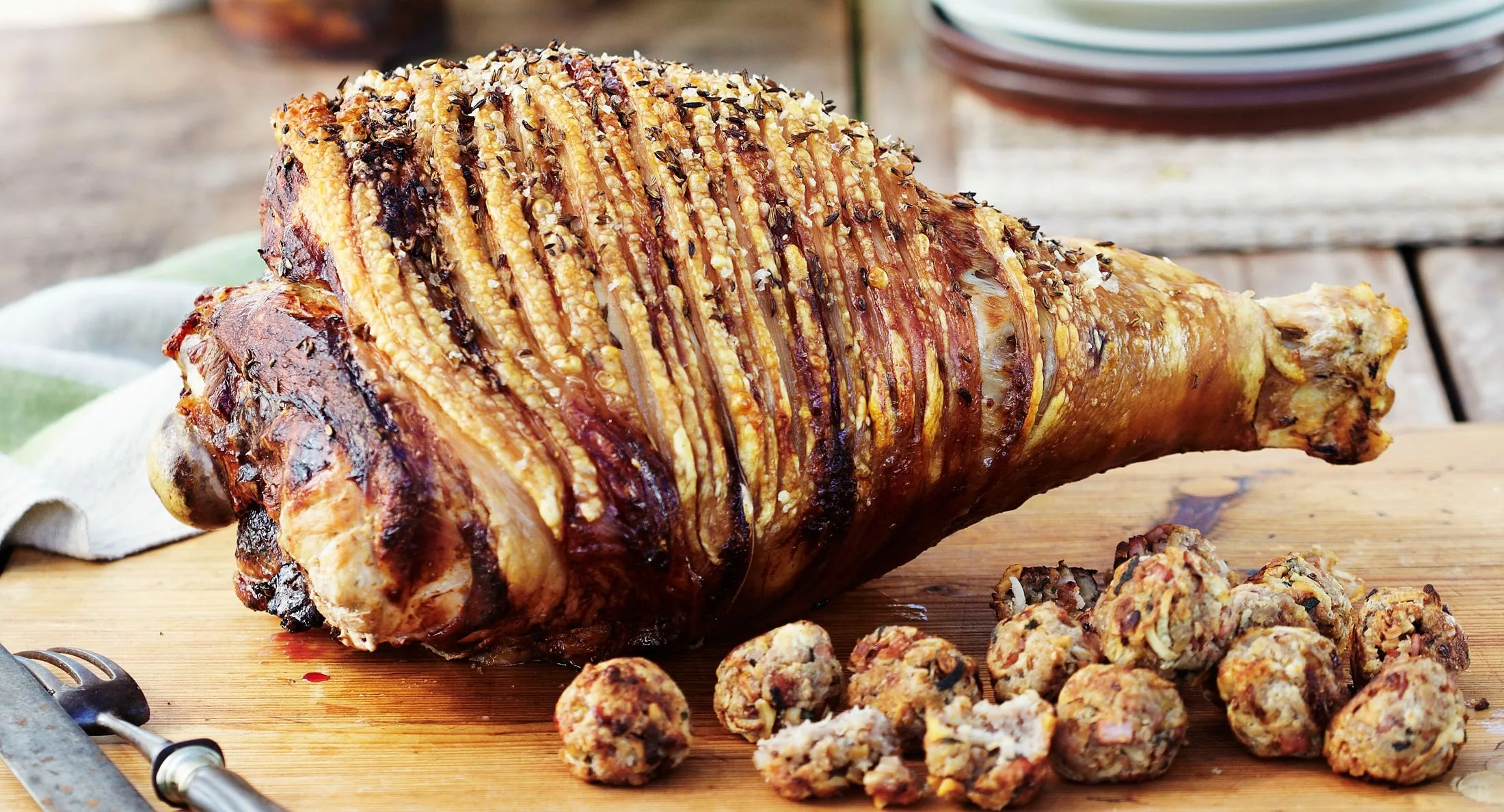 Roasted leg of lamb with crispy skin on a wooden board, served with small stuffing balls.