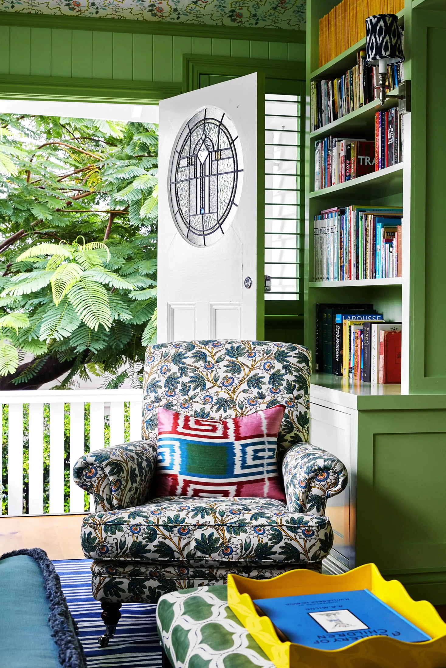 Green sunroom with floral upholstered chair and bookshelves