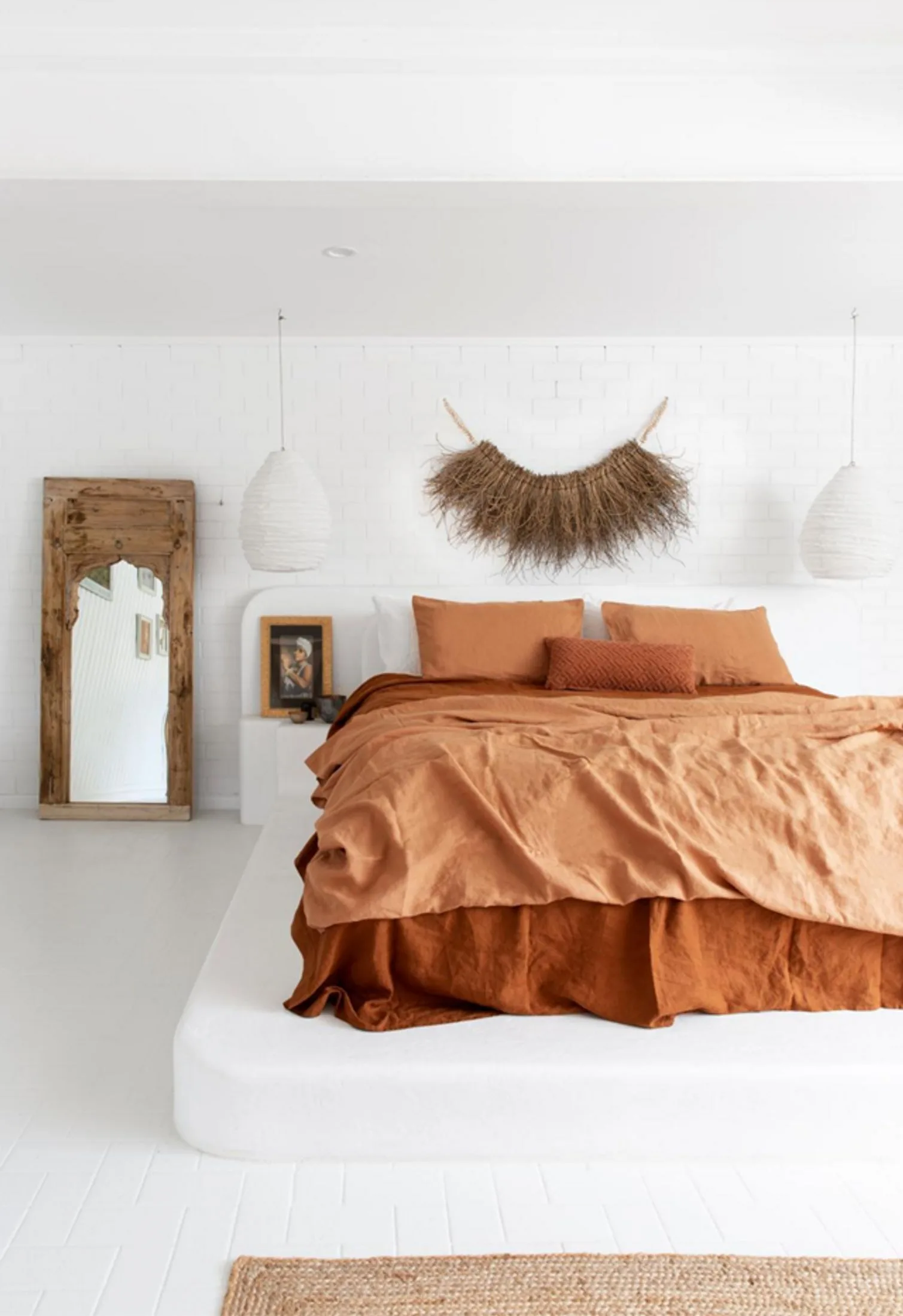 All-white bohemian style home with a bed dressed in terracotta linen