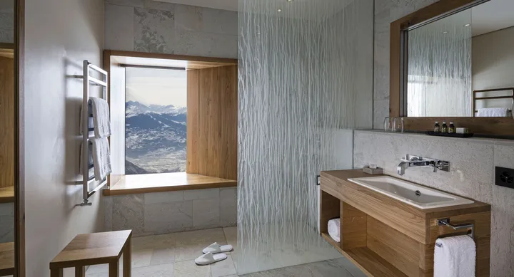 Modern bathroom with mountain view, wood accents, glass partition, towel rack, and slippers on tiled floor.