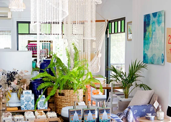 Cozy interior with plants, macramé decor, blue and white ceramics, and natural light through large windows.