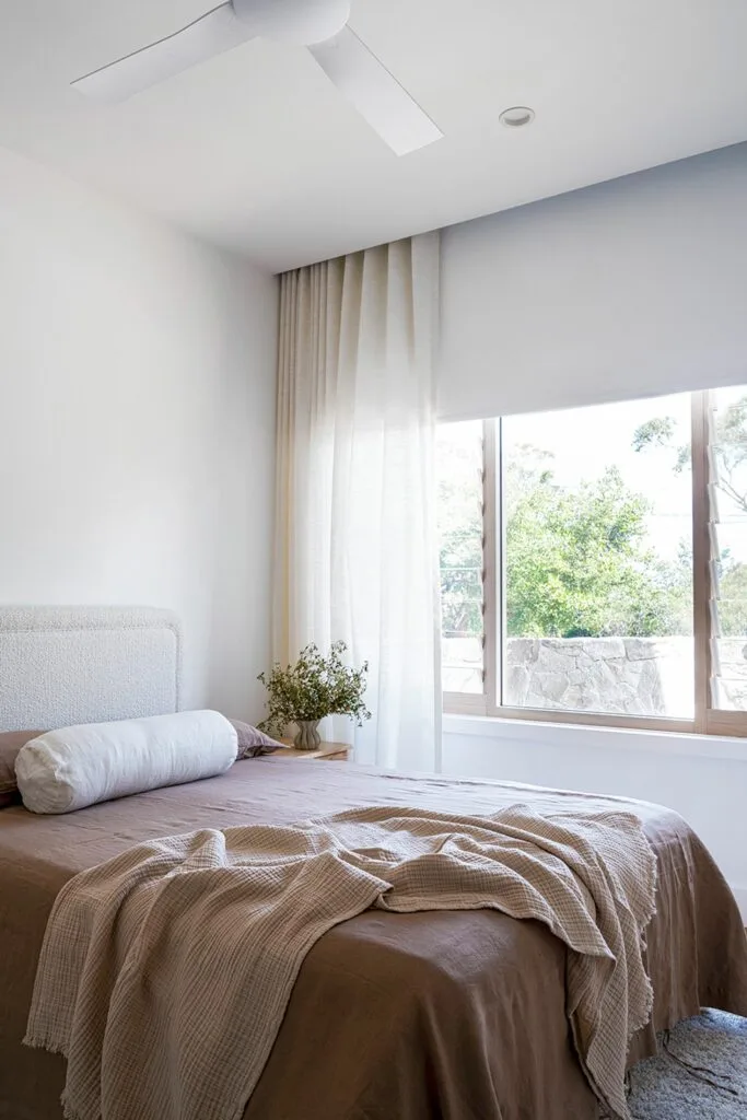 Contemporary neutral bedroom with ceiling fan and roller blind.