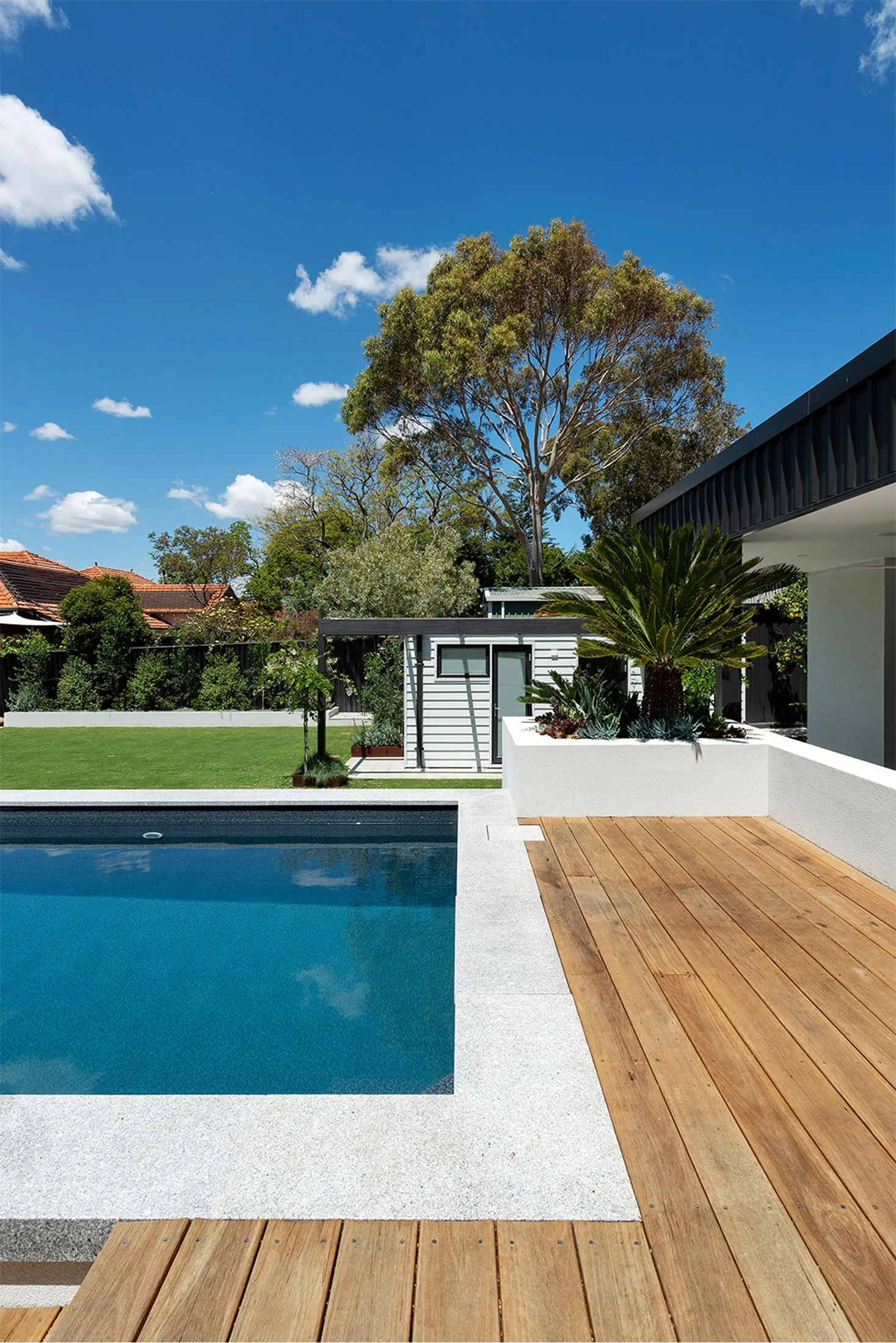 Outdoor pool and deck with a small white weatherboard granny flat with a black timber awning