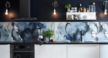 Modern kitchen with abstract blue backsplash, black countertop, blender, and shelves with dishes and spices.