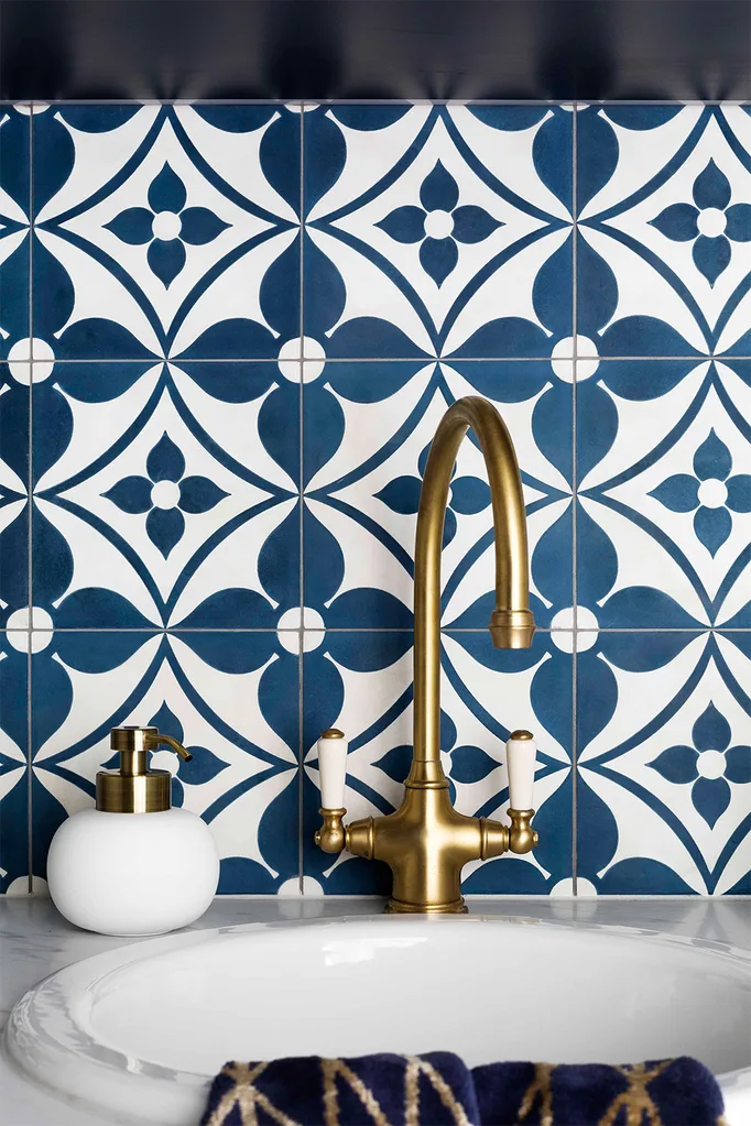 Tiny sink with blue patterned tile splash back and gold gooseneck tap.