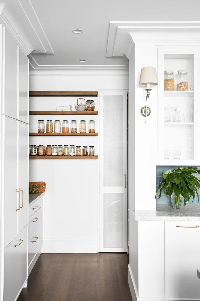 White and gold kitchen with oak floating shelves holding spices