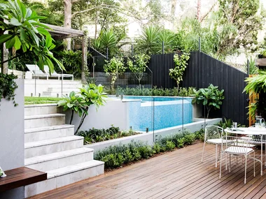 Backyard with pool next to a deck with a dining table and chairs.