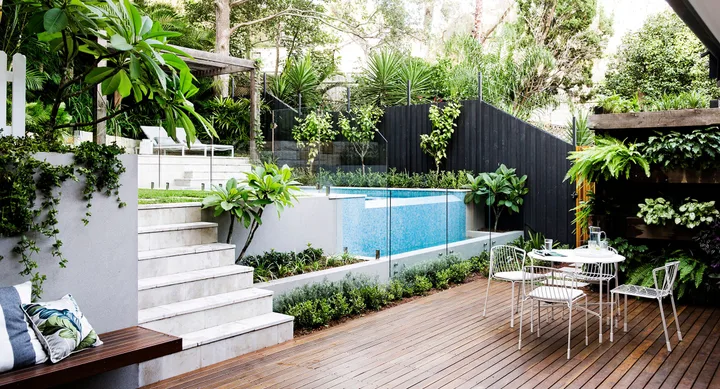 Backyard with pool next to a deck with a dining table and chairs.