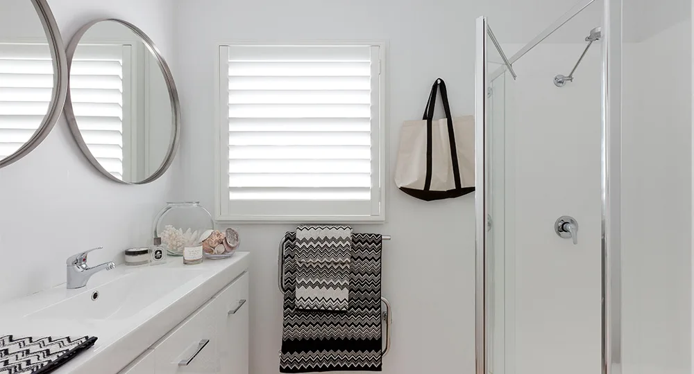 Bright modern bathroom with white sink, round mirrors, towel rack, and glass shower.