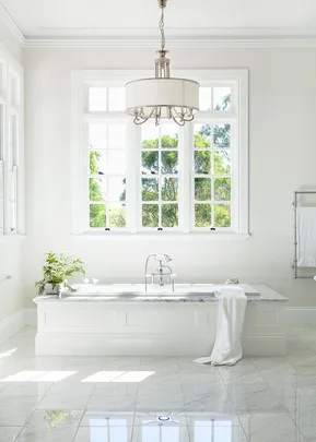 Elegant bathroom with a white marble tub, large windows, and a hanging chandelier, creating a bright and airy space.