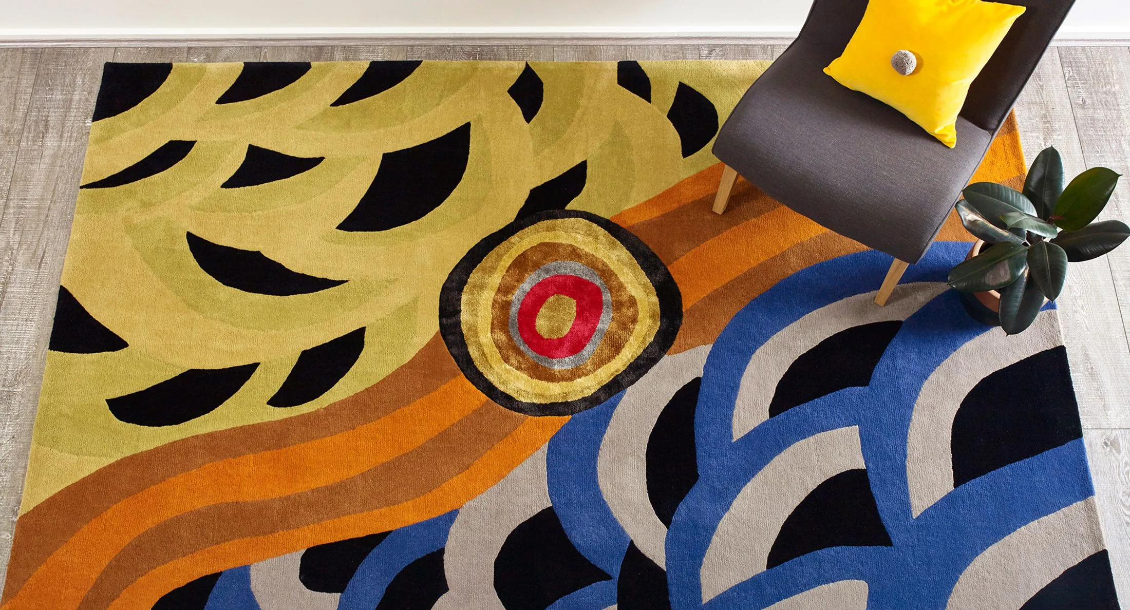Colorful abstract rug with dark chair, yellow cushion, and plant on wooden floor.