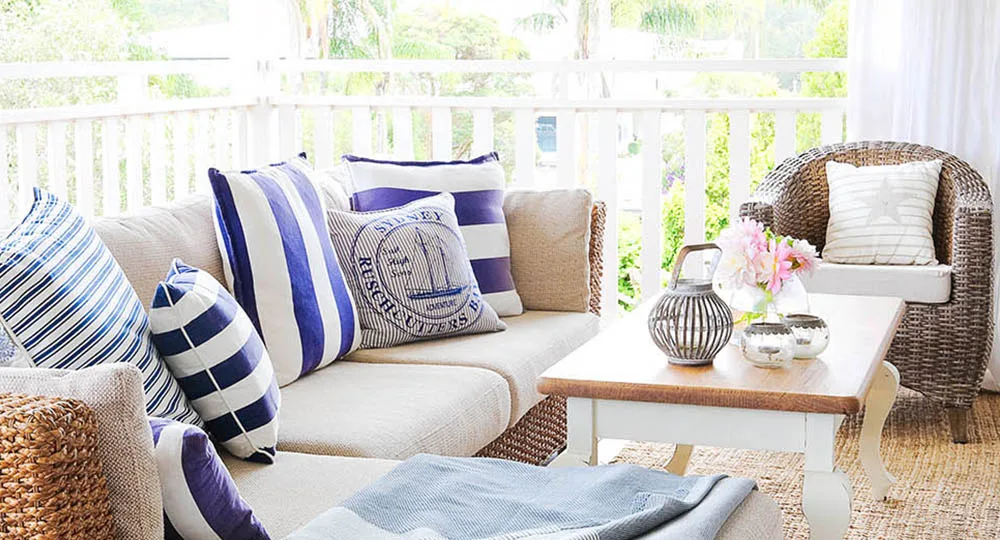 Cozy patio seating with striped cushions, a wicker chair, and a wooden coffee table adorned with lanterns and flowers.