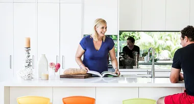 Two people in a bright kitchen; a woman reads a magazine, and a man sits at the counter.