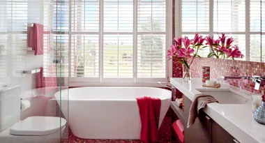 Luxurious bathroom with freestanding tub, pink towels, large windows, and fresh lilies in a vase on the counter.