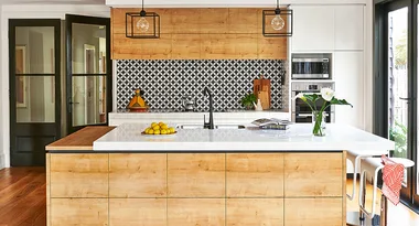 Modern kitchen with a large island, wood cabinetry, geometric backsplash, pendant lights, and fruit bowl centerpiece.
