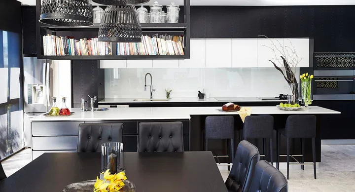 Modern kitchen with black and white theme, large countertop, pendant lights, bookshelves, and decorative items.