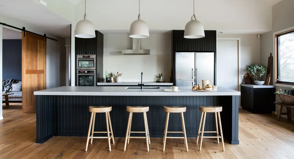 Modern kitchen with black cabinets, wood floor, island with stools, pendant lights, and stainless steel appliances.