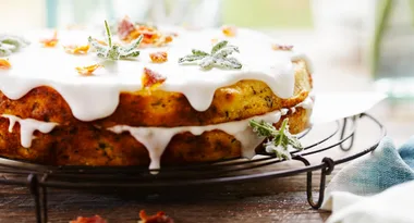 Layered cake with white icing and sugared leaves on top, resting on a wire rack.