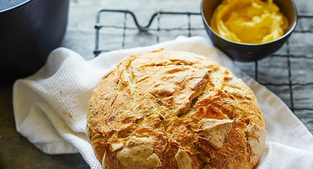 Crusty loaf of bread on a white towel with a bowl of butter in the background.