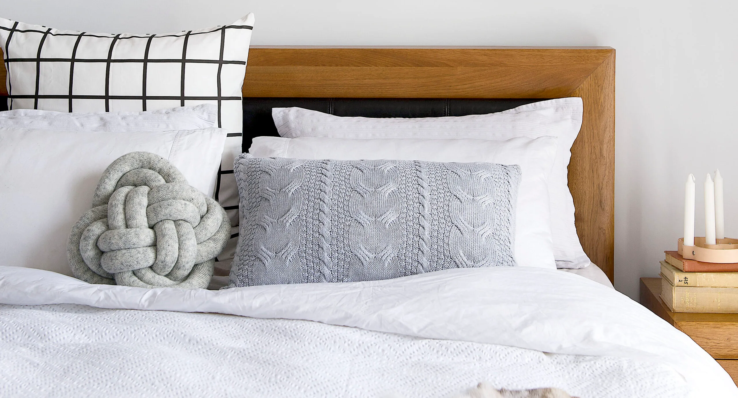 Bed with patterned pillows, wooden headboard, and side table with candles and books.