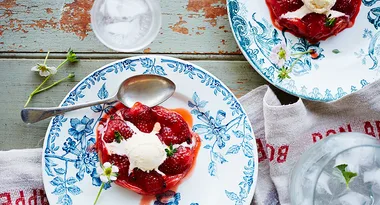 Strawberry dessert with ice cream on floral plates next to a glass of water and a napkin on a rustic table.