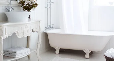 Elegant white bathroom with a freestanding clawfoot bathtub, ornate vanity, and fresh flowers on the counter.