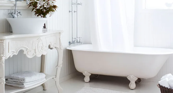 Elegant white bathroom with a freestanding clawfoot bathtub, ornate vanity, and fresh flowers on the counter.