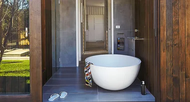 Outdoor freestanding bathtub with a striped towel, sandals, and trees in the background.