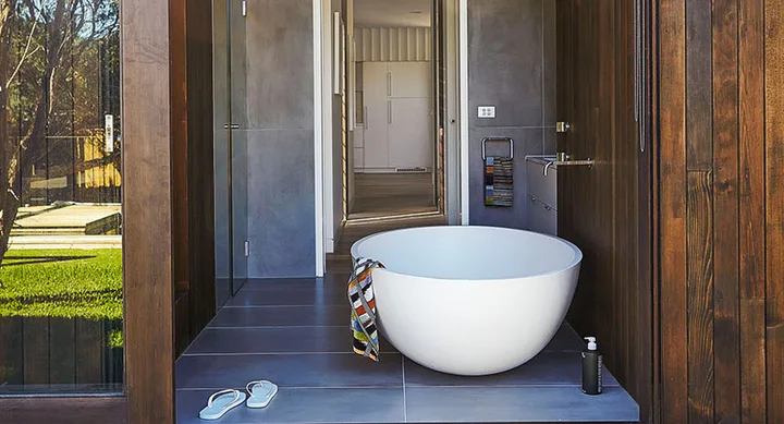Outdoor freestanding bathtub with a striped towel, sandals, and trees in the background.