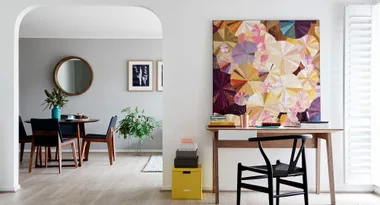Modern living room with dining area, art piece on wall, and desk with chair, all in soft neutral tones.